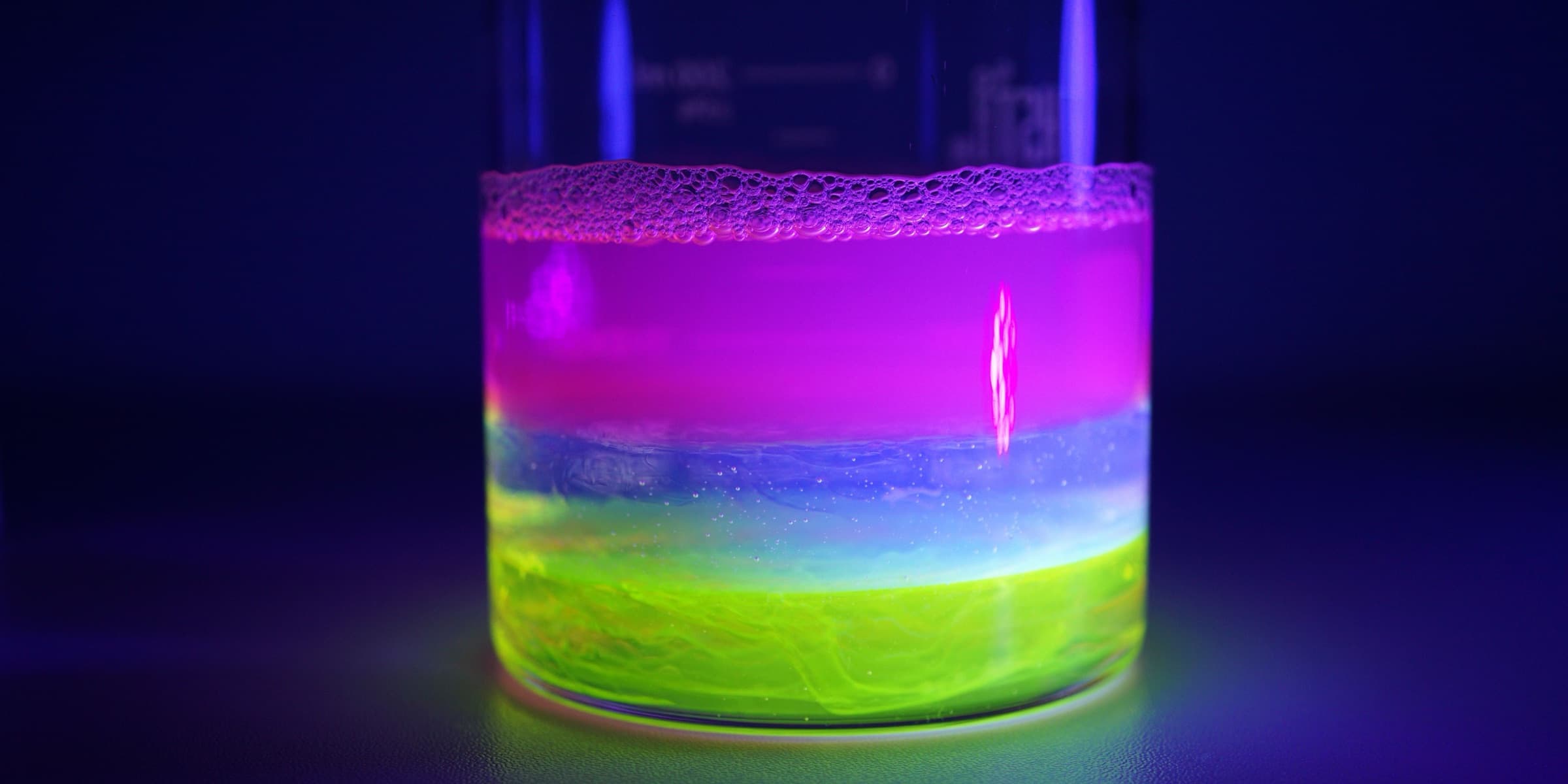 Fluorescent liquids glowing in a beaker under UV light